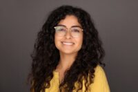 Woman with curly hair and glasses wearing a yellow shirt